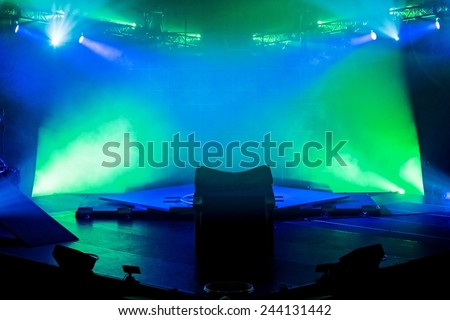An empty performance stage with green and blue lights lighting the area.
