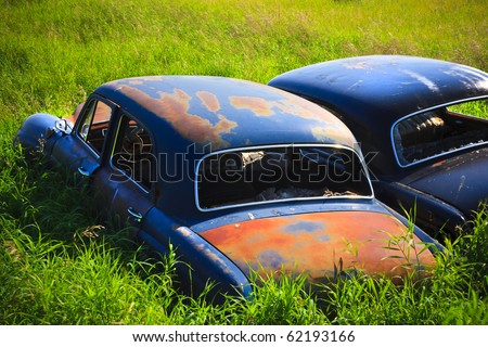 stock photo Old abandoned car rusting in the tall green grass