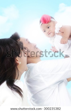 Portrait of happy family outdoor recreation. Dad hold her cute baby daughter up in the air, over blue sky background