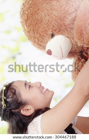 Beautiful scene of happy Asian girl playing with her teddy bear doll in the nature daylight
