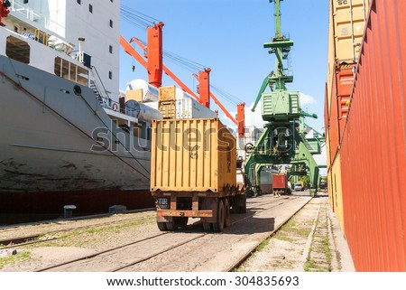 Cargo truck, loaded with container, is driving to a unload point next to massive port crane, at container terminal at Varna port, Varna, Bulgaria, May 16, 2014.