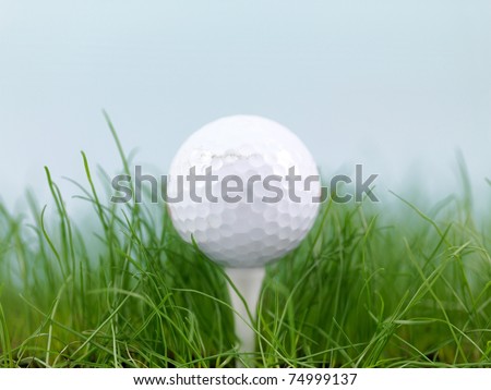 A golf ball on green grass isolated against a blue sky
