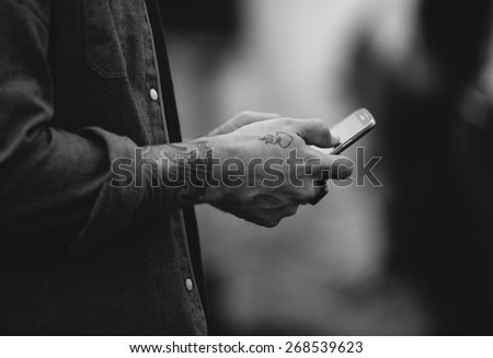 Close-up of hands with a heart tattoo holding a cellphone, possibly calling or messaging a loved one, or connecting on social media