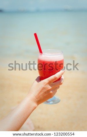 Woman holding fresh fruit cocktail on a tropical island beach