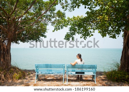 Young woman sitting on bench facing the sea in Thailand