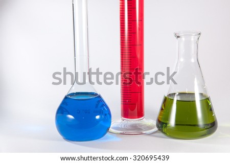 Picture showing some chemistry lab glassware: (from left to right) a volumetric flask with blue liquid, a graduated cylinder with a magenta liquid, an erlenmeyer flask with a green liquid.