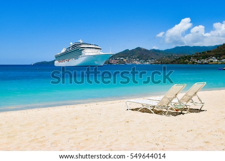 Cruise ship in Caribbean Sea with beach chairs on white sandy beach.\
Summer travel concept.