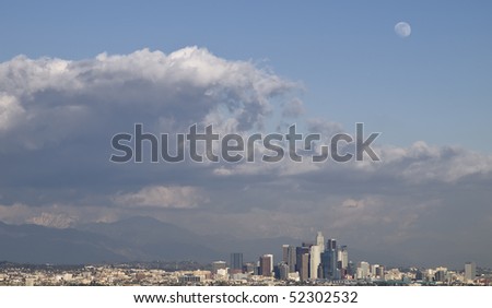 stormy clouds hoovering over downtown Los Angeles on a late winter afternoon,with a wolf-moon in the sky,and snow covering the san bernardino mountains in the background.