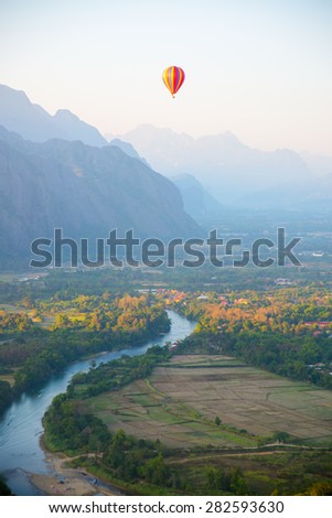 Striped hot air balloon flying over earth, evening landscape and the city with little houses, a river in Laos to Vang Vieng.Laos.