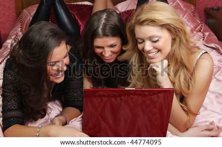 three teenage girls having fun with a laptop on the bed
