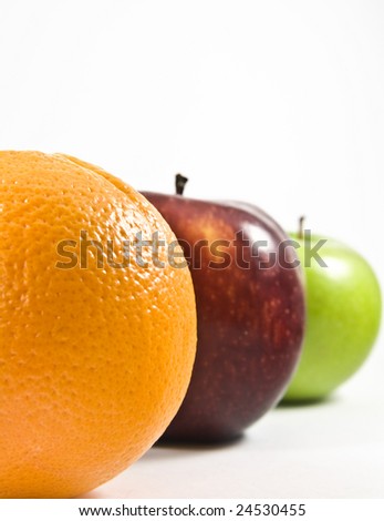 an orange, red apple and green apple lined up showing half of their shapes; the focus is on the orange while the rest are slightly blurred