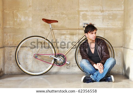 Young man sitting in front of his fixed-gear bicycle, also called fixie