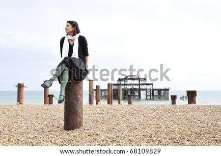Young asian woman sitting on a pole in front of the west Pier in Brighton, UK