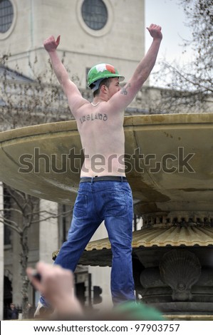 LONDON - MARCH 18: A shirtless man dancing on a fountain during the St Patrick\'s Day Parade and Festival at Trafalgar Square on March 18, 2012 in London, UK.