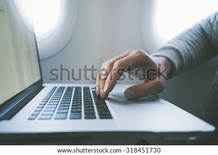 Man\'s hand typing on laptop at airplane