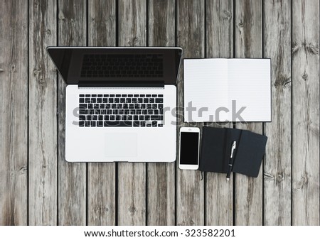 Mock up of workspace on wooden desk with laptop and white smartphone with blank screen, open notebook