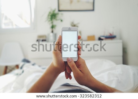 Close up of a man\'s hands using white smartphone with blank screen while lying in bed at morning