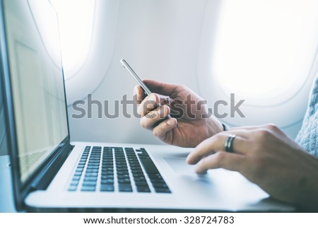 Side view of businessman using modern smartphone and open laptop at airplane
