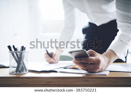 Close up of businessman using smartphone and working on documents at office, success man employer in office interior with cellphone and contract on desk