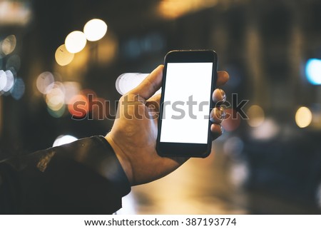 Closeup of male hand holding modern smartphone with blank screen for your text message or content, man\'s hand using cellphone with empty display at night city, bokeh light