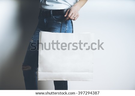 Close-up of female hand holding blank white paper package on white background, mock-up of white shopping bag with handles
