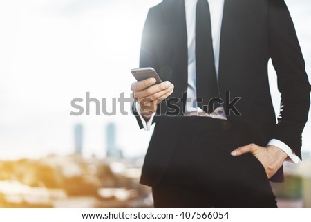 Young businessman wearing modern suit and using smartphone outdoors, professional male employer using mobile phone while working at office, blurred background with copy space for content or design