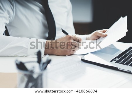 Professional banker working at his office with documents and using modern laptop computer, close-up of male hands signing contract