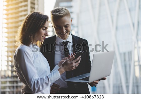 Happy smiling businessman and businesswoman using laptop and smartphone while working on new project, two young professional employers working on portable computer discussing project of constructions