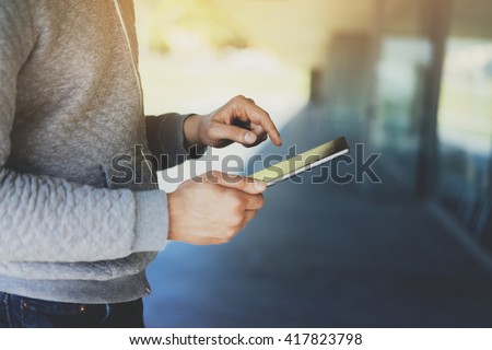 Close-up of male hands using digital tablet outside, young hipster man working or typing on touch screen of tablet pc near modern office, flare light