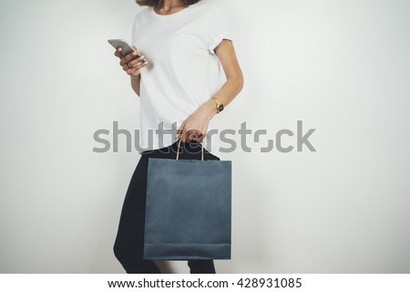 Young hipster girl wearing white t-shirt and holding blank blue shopping bag, mock-up of blue paper package, white background