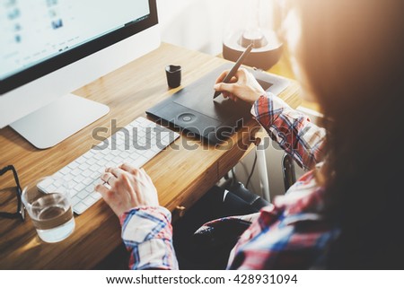 Young hipster graphic designer woman using digital graphic tablet while working at modern office, professional female retoucher sitting at modern workspace with wooden table, generic design tablet