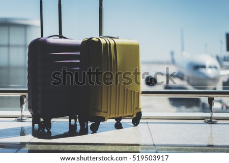 Two suitcases in the airport departure lounge, airplane in the blurred background, summer vacation concept, traveler suitcases in airport terminal waiting area, empty hall interior with large windows