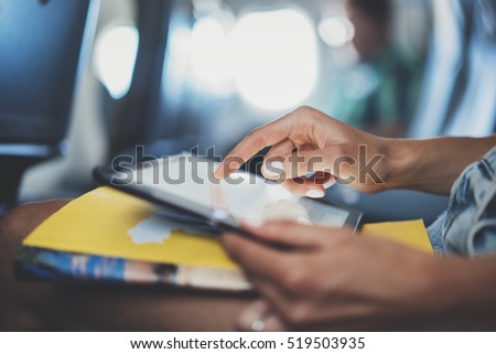Closeup of female hands typing text information on digital tablet device while sitting at airplane, young female traveler using tablet pc while waiting her take off on aircraft, inside airplane cabin