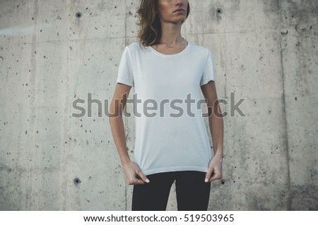 Pretty young girl wearing blank white t-shirt with area for your logo or design, mock-up of template white t-shirt, concrete wall in the background