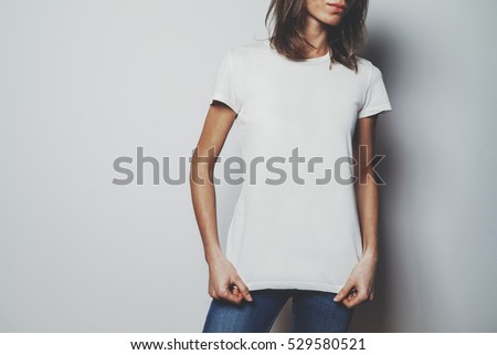 Young hipster girl wearing blue jeans and blank white t-shirt with area for your logo or design, mock-up of white t-shirt, white wall in the background