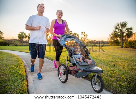 Couple exercising and jogging together at the park pushing their baby in a stroller