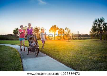 File name:Beautiful, fit young family walking and jogging together outdoors along a paved sidewalk in a park pushing a stroller at sunset