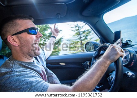 Happy man enjoying a road trip in his car on a sunny day. Singing and listening to music in his car on a scenic drive