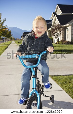 Little boy learning to ride a bike with training wheels