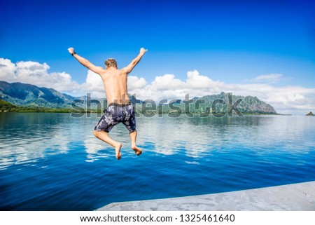 Man jumping into the ocean while on a beautiful scenic Hawaiian vacation. Thrilling and exciting experience. Concept about holiday, success, accomplishment and lifestyle