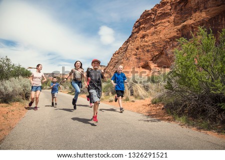 A large group of smiling kids running together on a pathway at a national park. Having fun out in nature during a summer vacation. Active, happy boys and girls