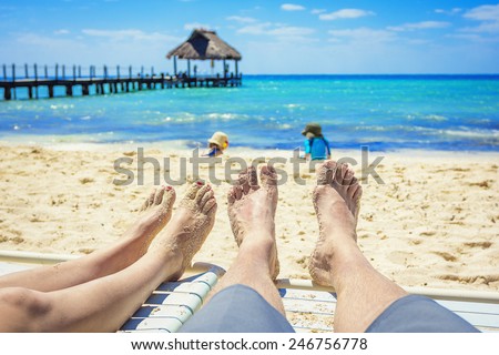 Tan Feet of a couple on lounge chairs enjoying a beach vacation while watching their kids play in the sand