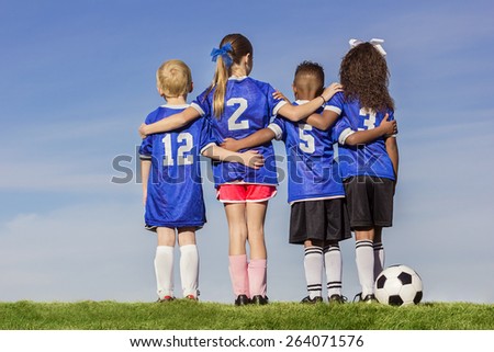 Diverse group of boys and girls soccer players standing together with a ball against a simple blue sky background