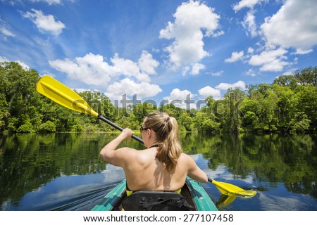 Woman kayaking along a beautiful tropical jungle river. Lots of copy space above and view from behind