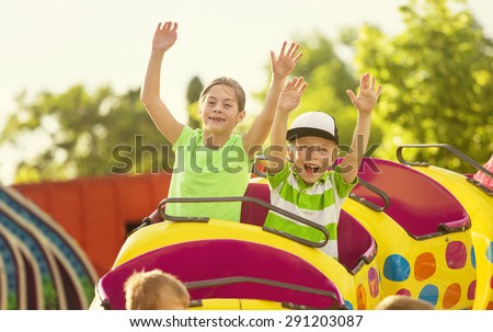 Boy and Girl on a thrilling roller coaster ride at an amusement park with arms raised and yelling with excitement