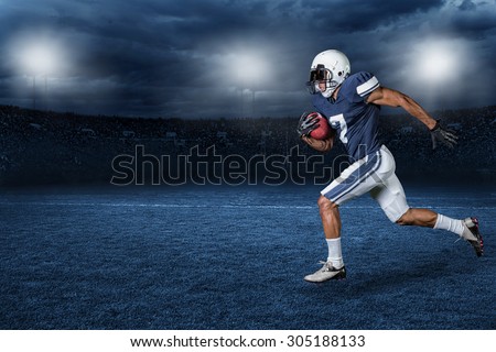 American Football Player Running for a touchdown in a large outdoor professional football stadium at night