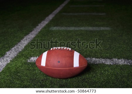 Football resting on a turf field at night. Lots of copy space with dramatic lighting