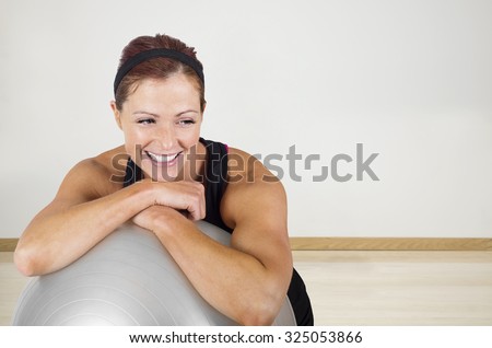 Happy healthy fitness woman resting on a exercise ball. Candid portrait of a smiling woman resting after exercising at an indoor gym