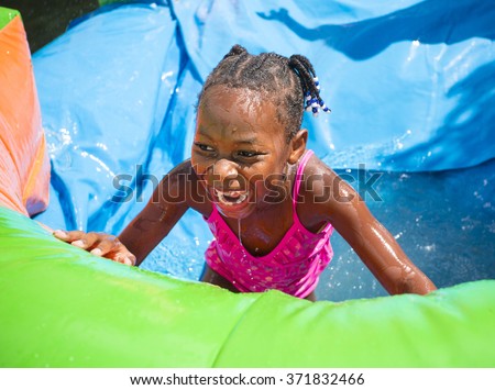 Smiling little girl playing outdoors on an inflatable bounce house water slide