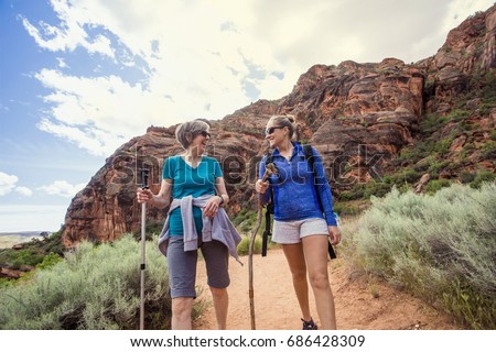 Two happy women hiking together in a red rock sandstone canyon in the deserts of Utah on an adventure vacation. Two women smiling and talking together during a fun hike